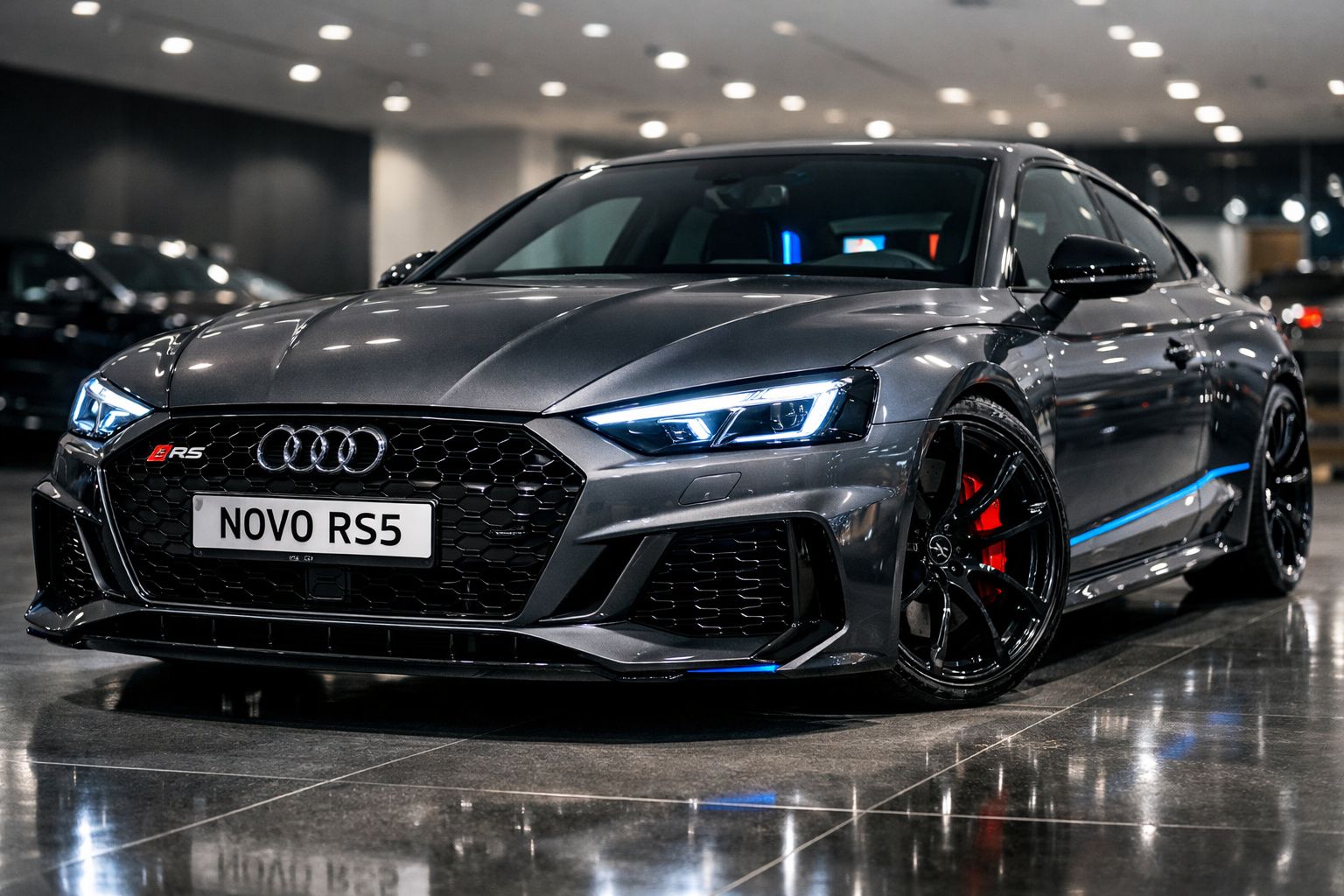 Automóvel Audi RS5 cinzento escuro com faróis acesos e jantes pretas, parado em piso interior reflectivo.